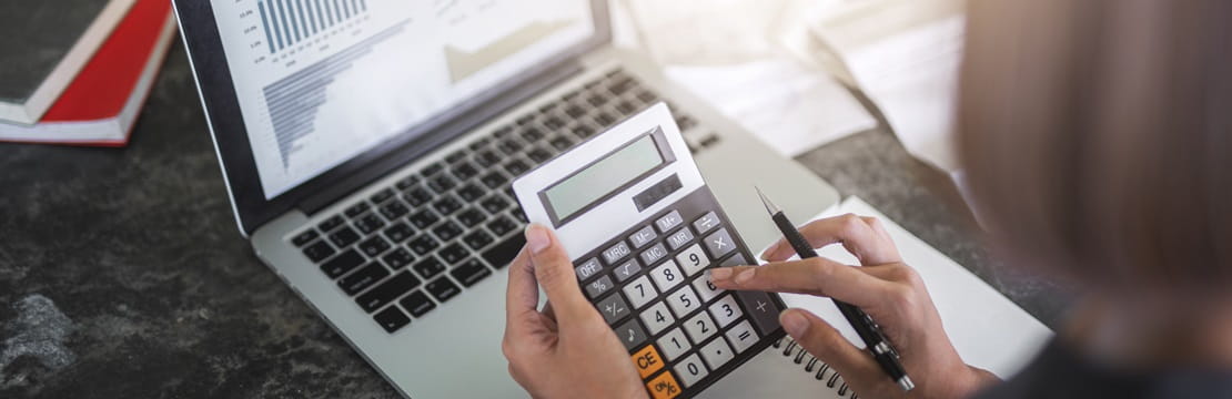 Woman's hands using a calculator while on her laptop computer.